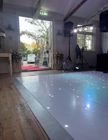 Una habitación con piso de madera pulida, un escenario con alfombra roja y un ventanal con luz natural.