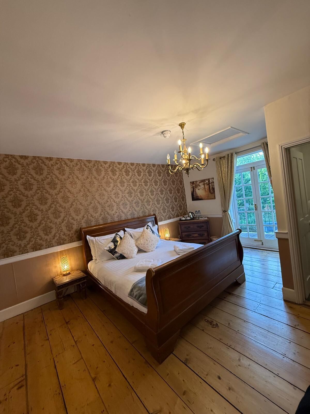 A bedroom with a wooden bed, a chandelier, a nightstand, and a window with curtains.