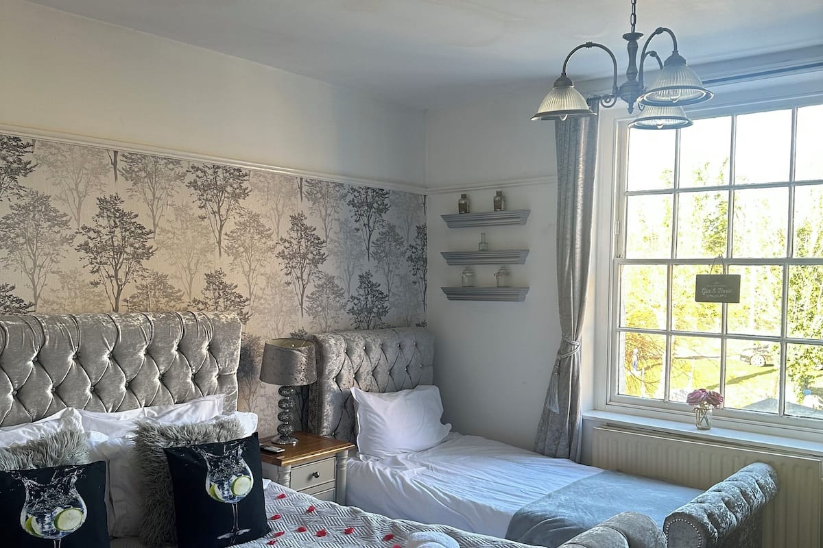 A bedroom with a large bed, a nightstand, a dresser, and a window with a view of greenery.