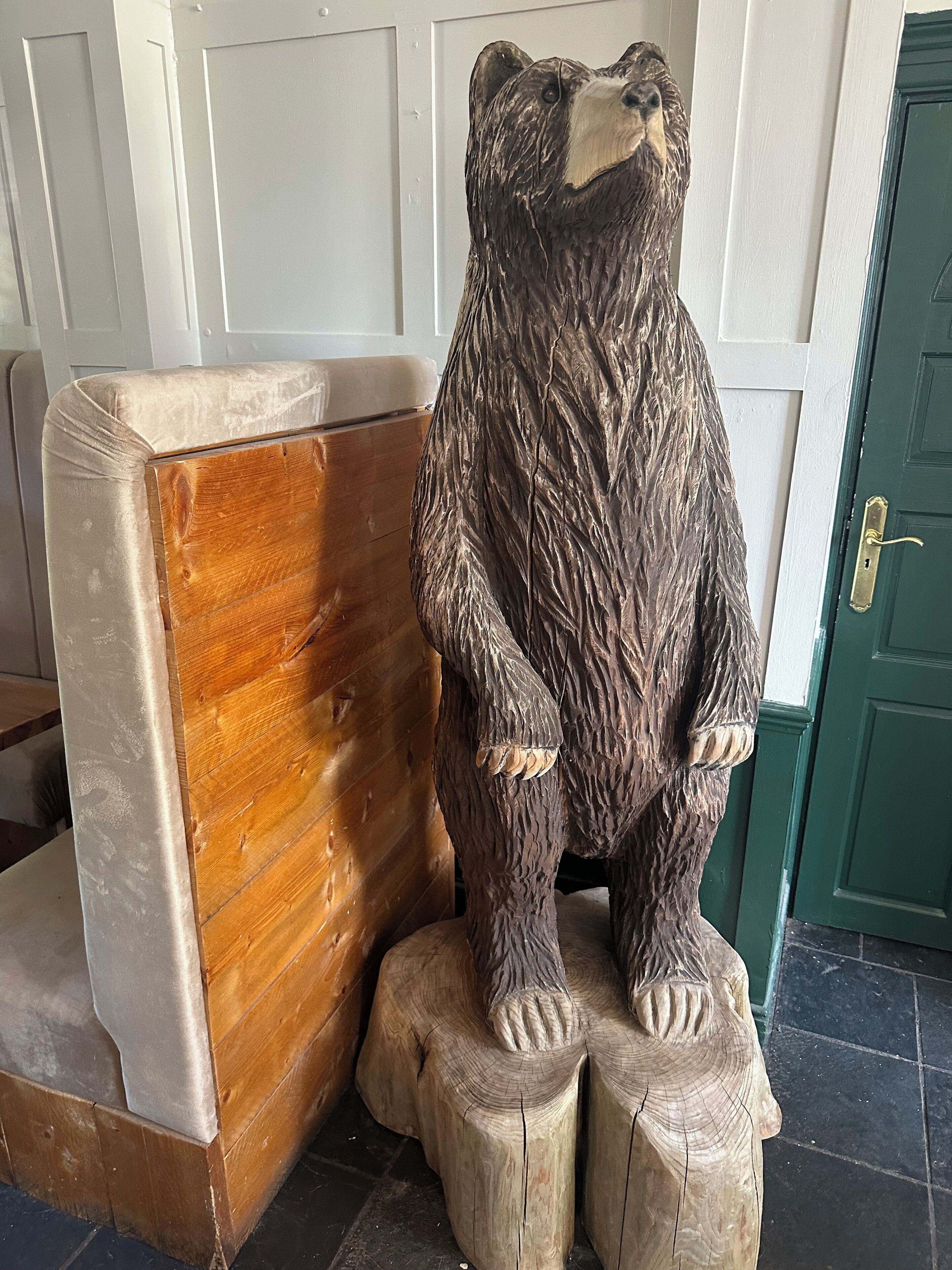 A wooden bear sculpture sitting on a wooden stump.