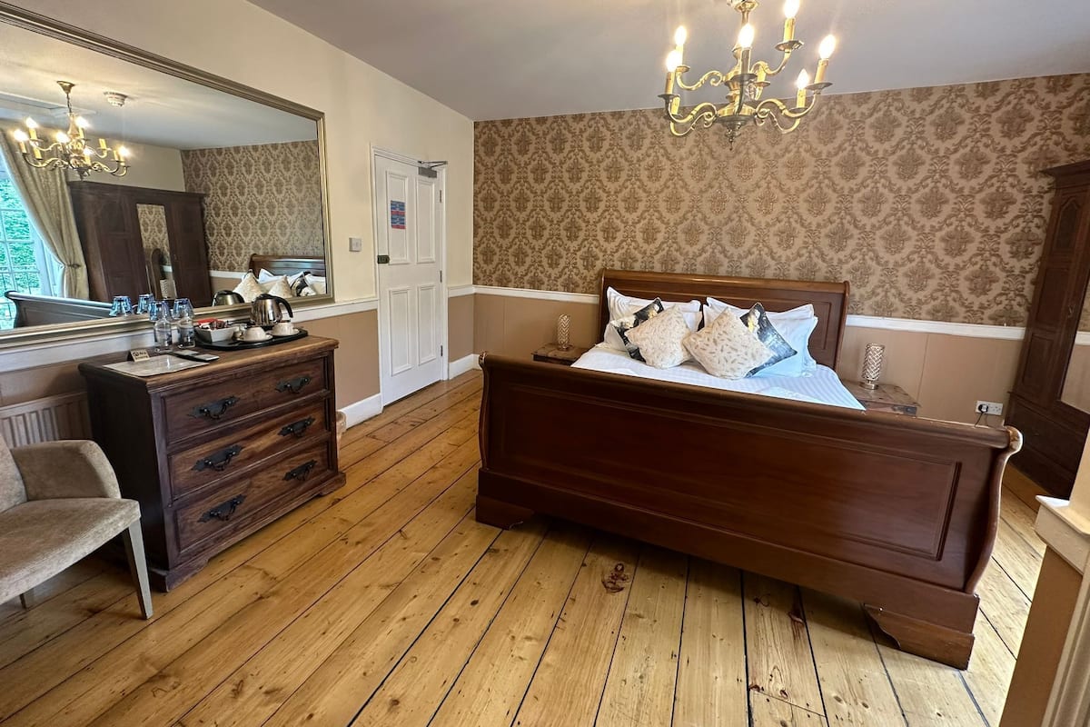 A bedroom with a wooden bed, a dresser, a mirror, and a chandelier.