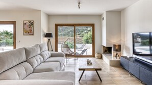 A modern living room with a sofa, a coffee table, a TV, and a balcony with a view. - Villa 'Maréa' with Sea Views, Wi-Fi, and Air Conditioning (Calonge)