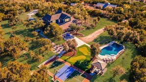 Vista aérea de una propiedad residencial con piscina, cancha de tenis y jardín ajardinado.