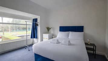 A hotel room with a large bed, a bedside table, a nightstand, a window with curtains, and a view of the outside.