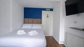 A hotel room with a bed, a TV mounted on the wall, and a door with an emergency exit sign.