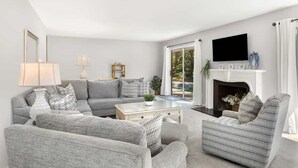 A living room with a sofa, armchairs, a coffee table, a fireplace, and a TV mounted on the wall. - Private Pool | Walk to Beach | 3BR Retreat (Hilton Head Island)
