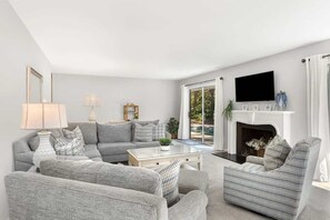 A living room with a sofa, armchairs, a coffee table, a fireplace, and a TV mounted on the wall. - Private Pool | Walk to Beach | 3BR Retreat (Hilton Head Island)