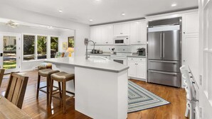 A modern kitchen with white cabinetry, a large island, stainless steel appliances, and a view to the outdoors. - Private Pool | Walk to Beach | 3BR Retreat (Hilton Head Island)