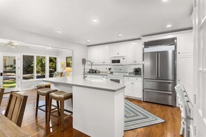 A modern kitchen with white cabinetry, a large island, stainless steel appliances, and a view to the outdoors. - Private Pool | Walk to Beach | 3BR Retreat (Hilton Head Island)