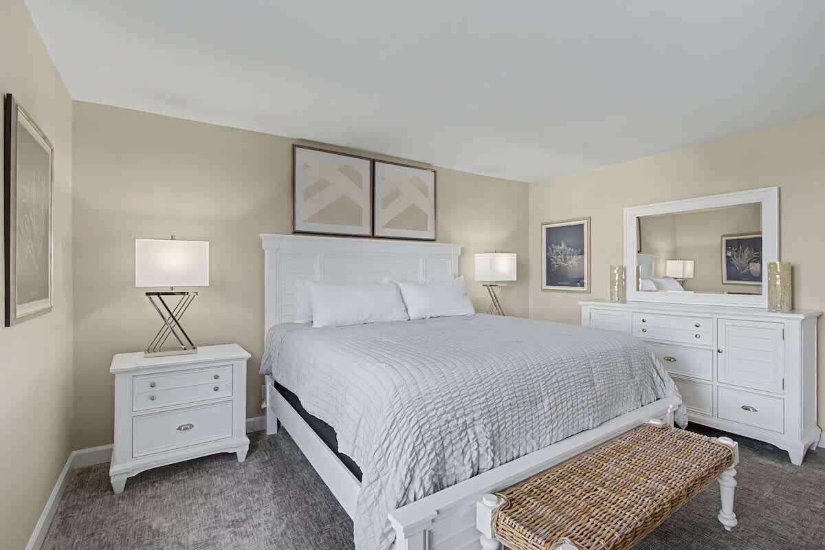 Une chambre à coucher comprenant un lit, des tables de chevet, un banc, une commode et un miroir.