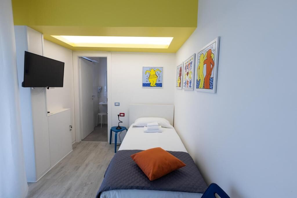 A bedroom with a bed, a TV mounted on the wall, and artwork on the walls.