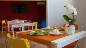 A dining area with a white table set for two, yellow chairs, and a television on the wall.