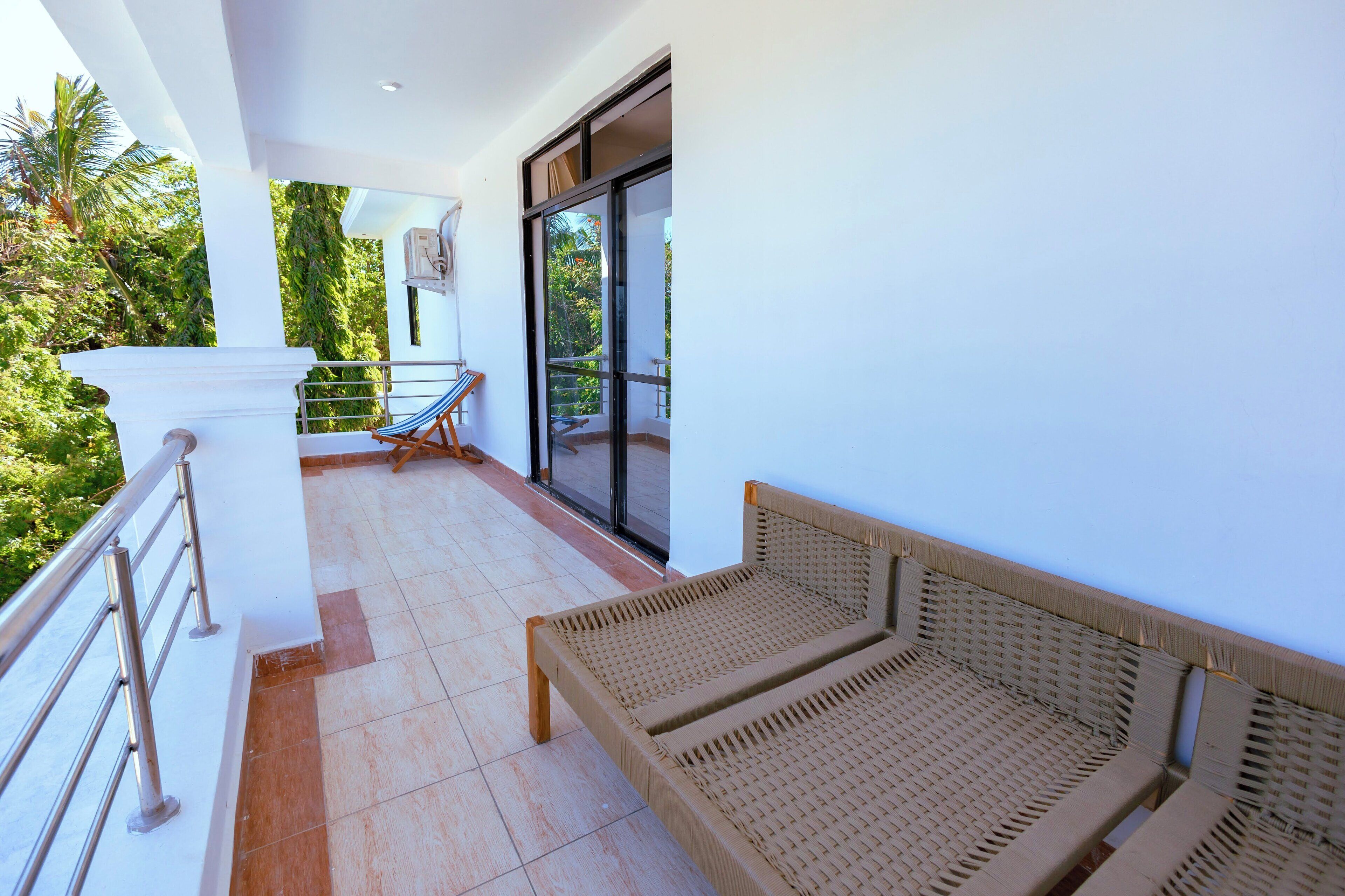 A balcony with a wicker sofa, a metal railing, and a view of greenery.