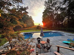 Piscina con área de terraza, rodeada de árboles y vistas al atardecer.