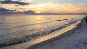 Ein Strand bei Sonnenuntergang, ruhiges Wasser und Fußabdrücke im Sand.