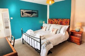 Un dormitorio con una pared verde azulado, una cama con ropa de cama blanca, una mesita de noche de madera y un cuadro colgado en la pared de una ballena.