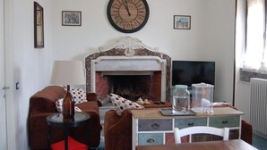 Una sala de estar con chimenea, un reloj, un sofá, un televisor y una mesa con varios objetos.