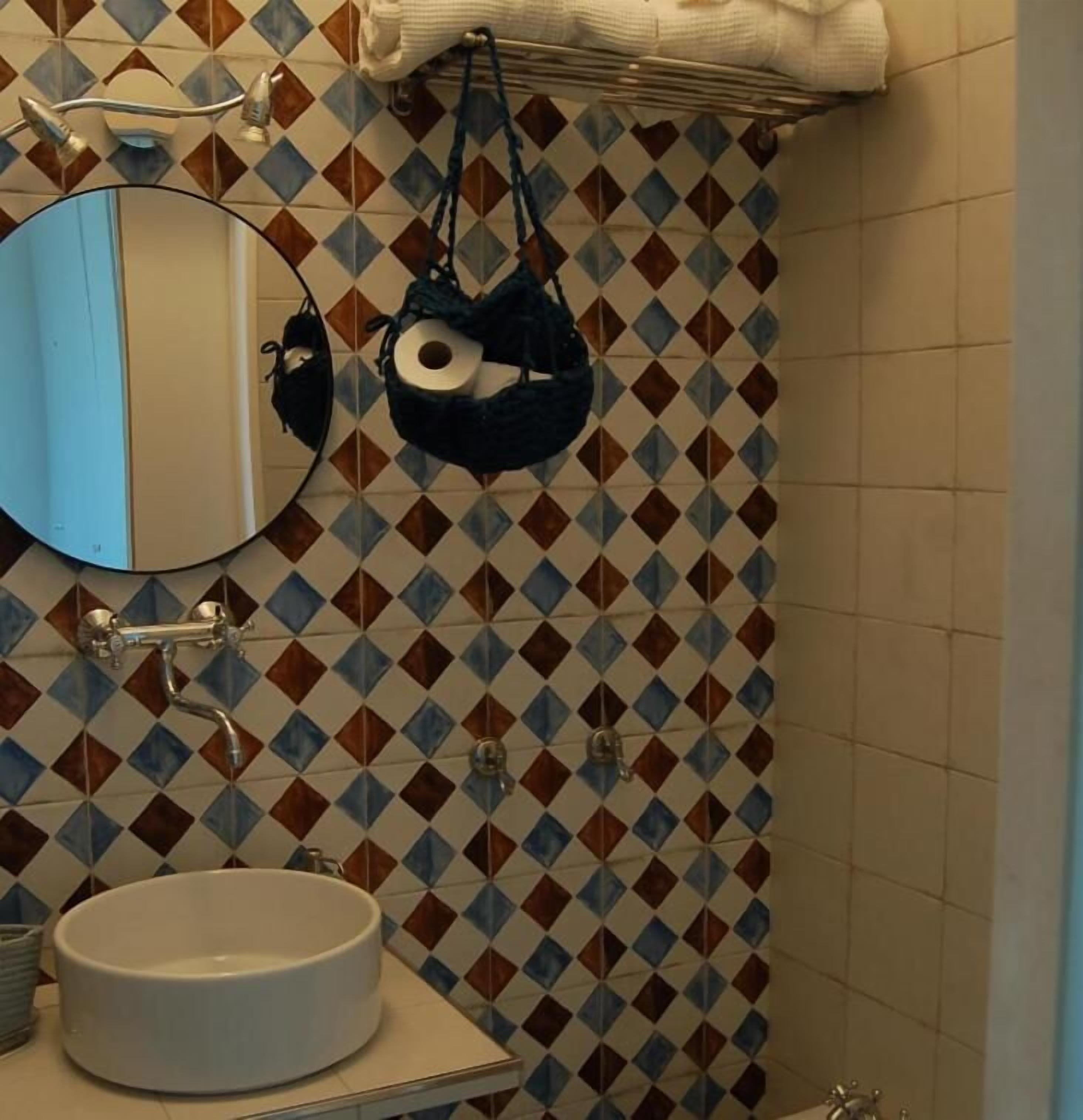 Ein Badezimmer mit einem Fliesenrückwand mit Muster, einem runden Waschbecken, einem Spiegel und einem Handtuchhalter.