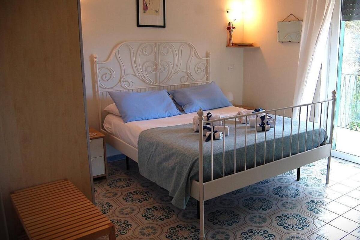 Un dormitorio con una estructura de cama metálica blanca, dos almohadas azules, una colcha verde y una mesita de noche.