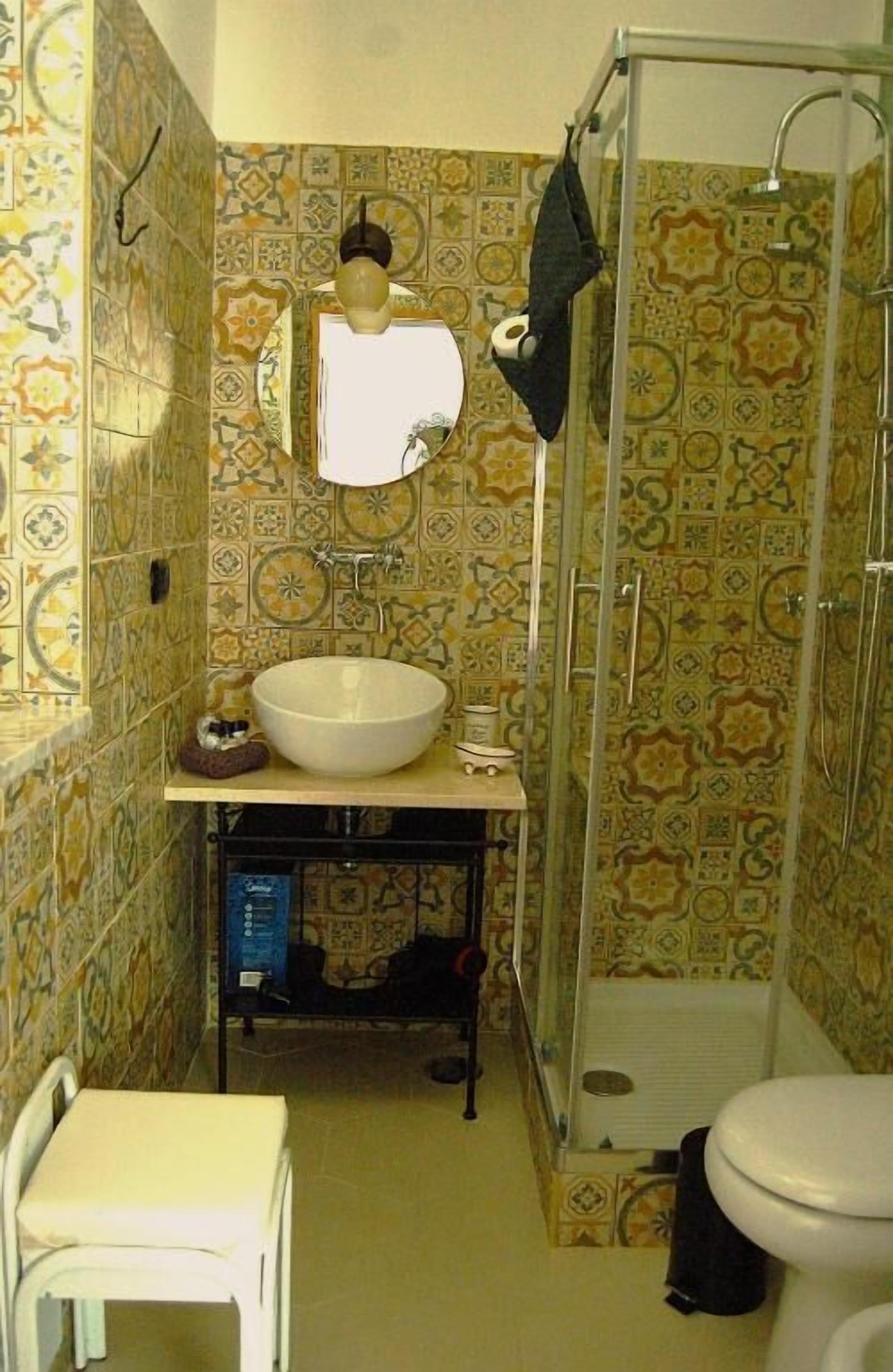 A bathroom with patterned tiles, a sink, a mirror, a shower, and a toilet.