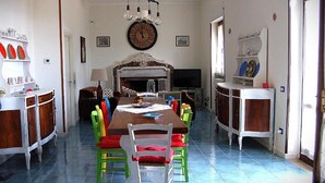 Un comedor con una gran mesa de madera, sillas coloridas, una araña y una chimenea.