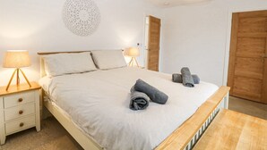 A neatly made bed with a light-colored duvet, two bedside lamps, a decorative wall piece, and two wooden doors. - The Ivy (Norwich)