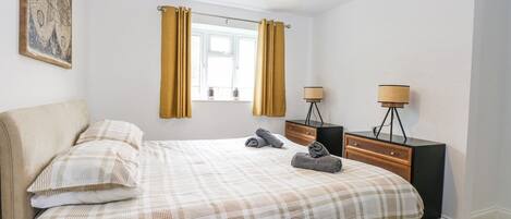 A bedroom with a bed, two bedside tables, a window with curtains, a hanging lamp, and a painting on the wall.