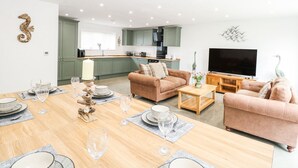 A modern living room with a dining area, a kitchen in the background, and a flat-screen TV. - The Ivy (Norwich)