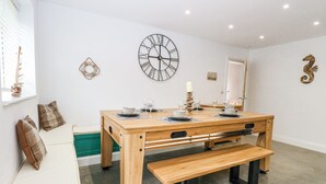 A dining area with a wooden table set for four, a bench, and a wall clock. - The Ivy (Norwich)