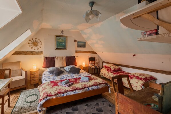 Ein gemütliches Schlafzimmer im Dachgeschoss mit schrägen Wänden, einem großen Bett mit gemusterten Textilien, einem Holztisch und einem Lesesessel.