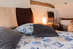 Ein Bett mit mehreren Kissen, ein Nachttisch mit Lampe und ein Sessel in einem Raum mit rustikalem Decken- und Wanddekor.
