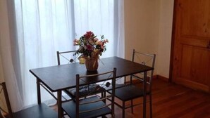 A dining table with four chairs, a vase of flowers, and a window with sheer curtains. - Lomas del Hualle - House 2 (Valdivia)