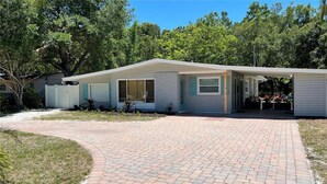 Una casa a un piano con portico coperto, vialetto in mattoni e giardino recintato.