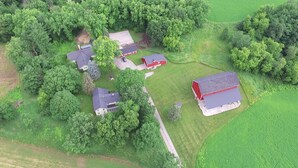 An aerial view of a rural property with multiple buildings, including a red barn, surrounded by dense green trees and fields. - Rubicon farmhouse minutes from Erin Hills Golf course, Holy Hill, & Bowery Barn (Rubicon)