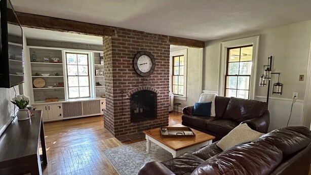 A living room with a brick fireplace, a brown leather sofa, a wooden coffee table, and a television on a stand. - Rubicon farmhouse minutes from Erin Hills Golf course, Holy Hill, & Bowery Barn (Rubicon)