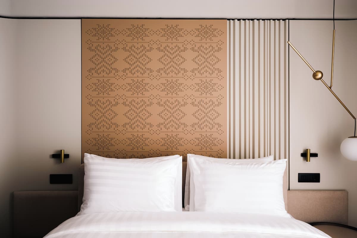 Una habitación de hotel moderna con una cama grande, un cabecero estampado, una lámpara de noche y una mesita de noche.