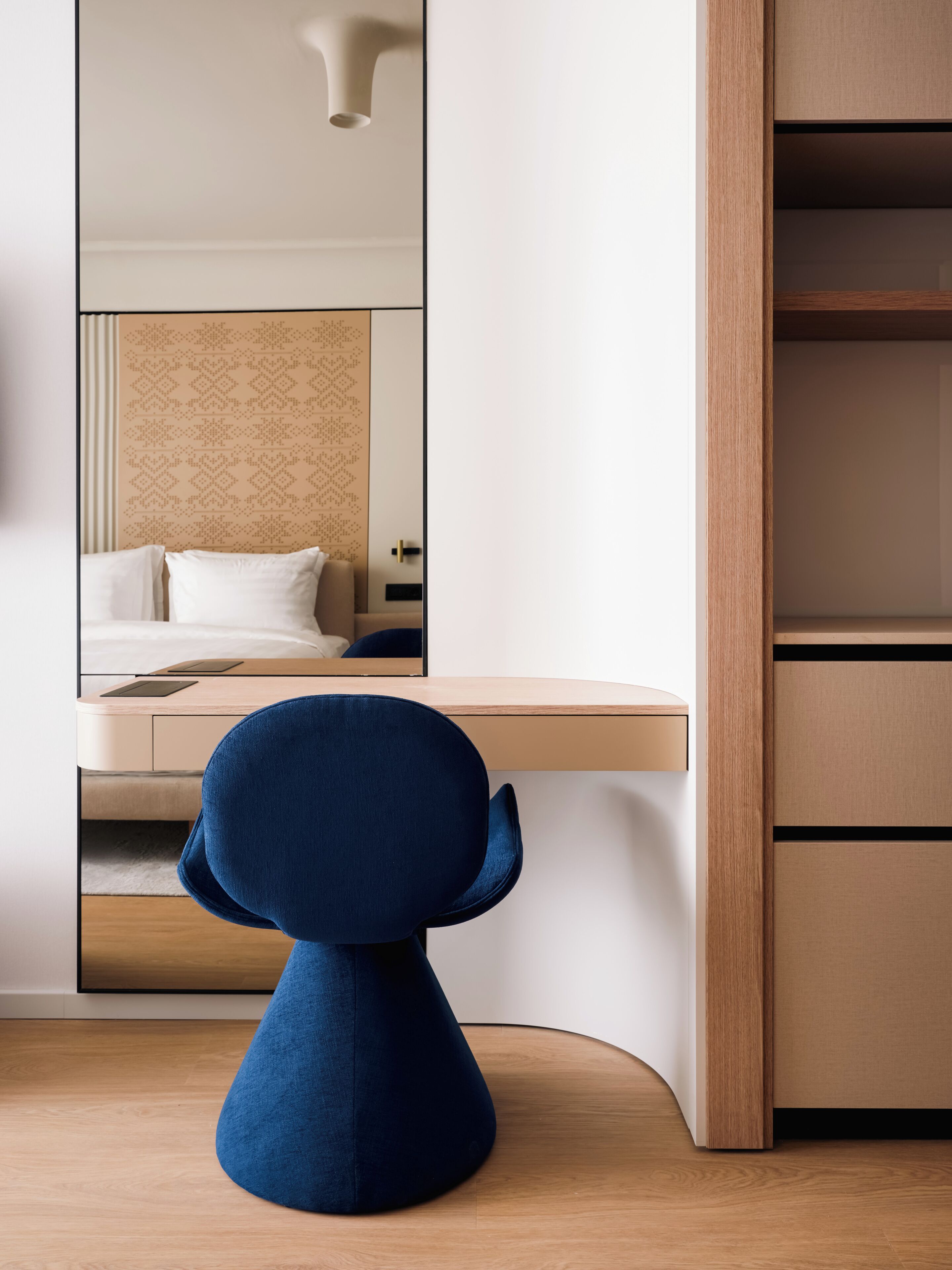 A modern room with a wooden desk, a blue chair, a bed with white bedding, and a wardrobe.