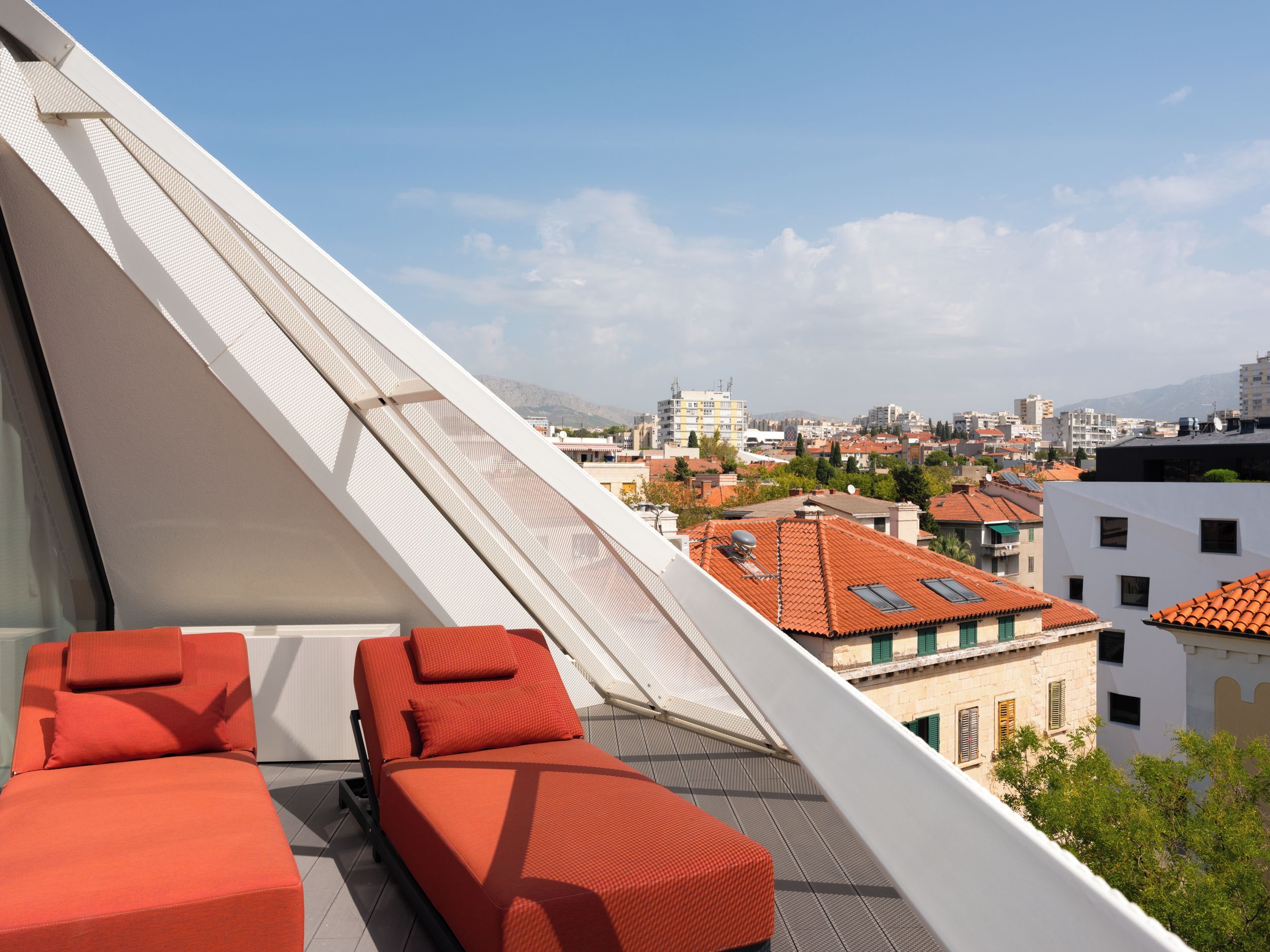 A rooftop terrace with two red lounge chairs and a white awning.