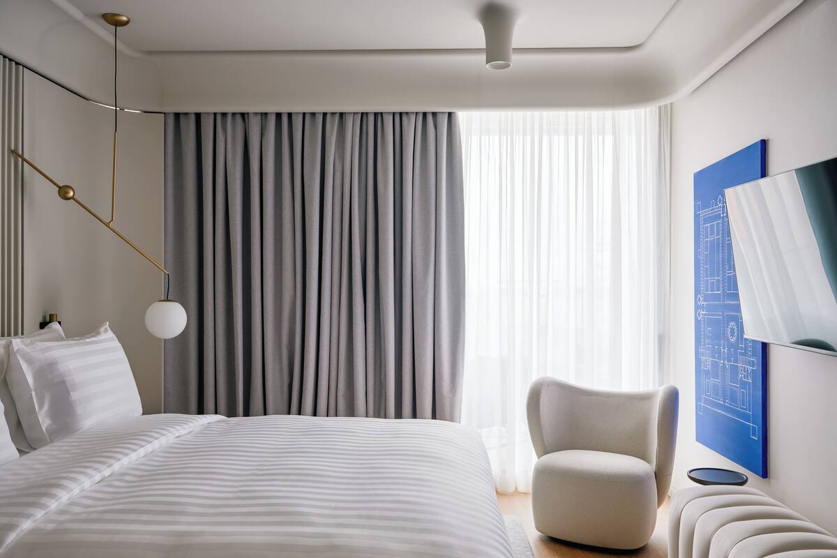 Habitación de hotel moderna con una cama grande, una silla, un escritorio y un ventanal con cortinas.