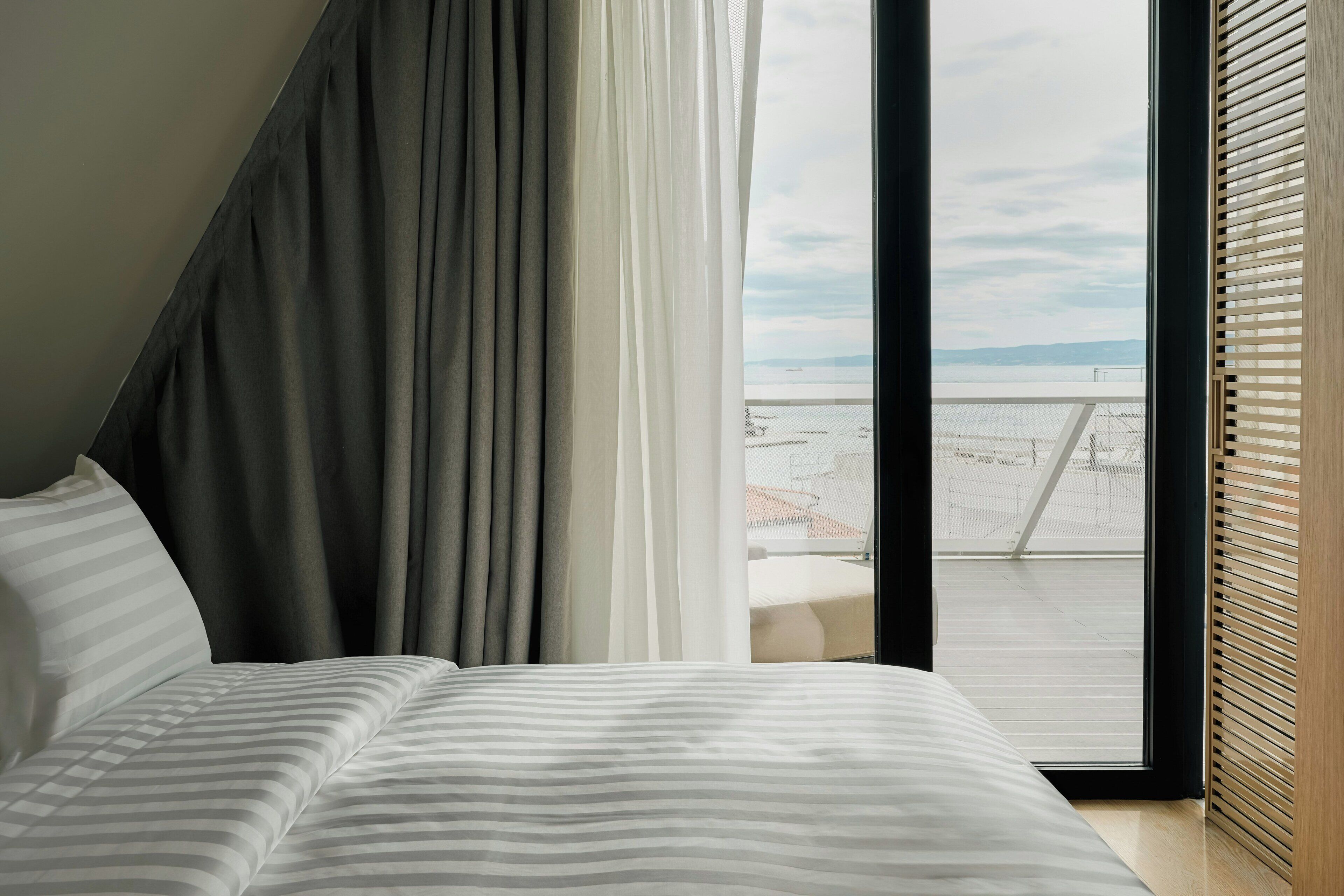 Una camera d'albergo con un letto, tende, una finestra vista un balcone e l'acqua.