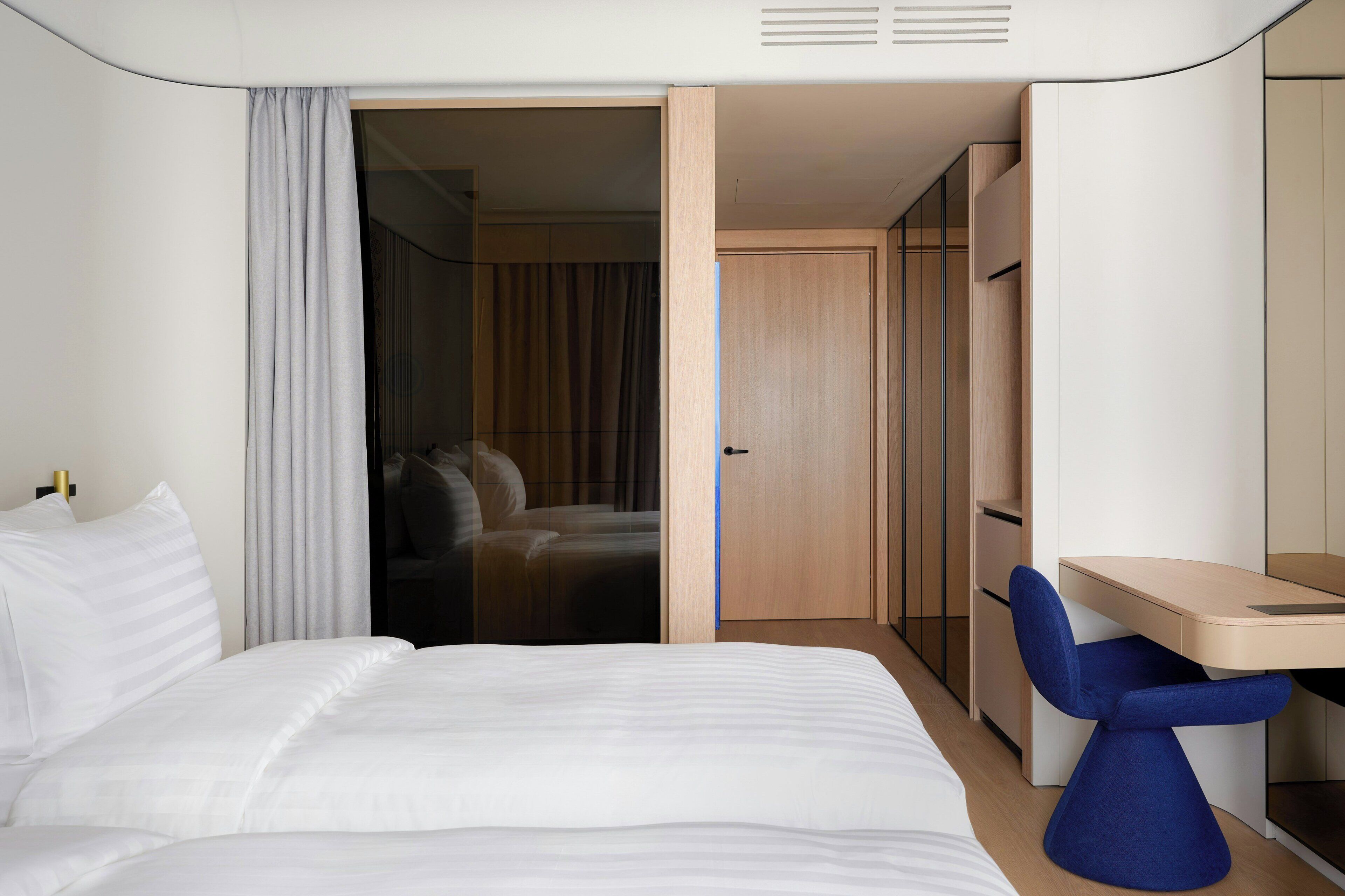 A modern hotel room with a bed, a desk, and a wardrobe.