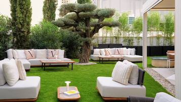 A modern outdoor living space with a sectional sofa, a coffee table, and a large tree.