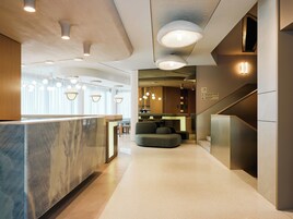 En moderne hotellobby med receptionsdisk, siddeområde og trappe.