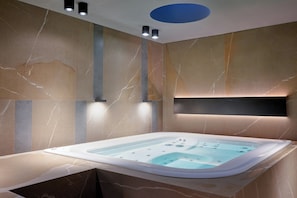 A modern bathroom with a freestanding bathtub, marble walls, recessed lighting, and a built-in shelf.