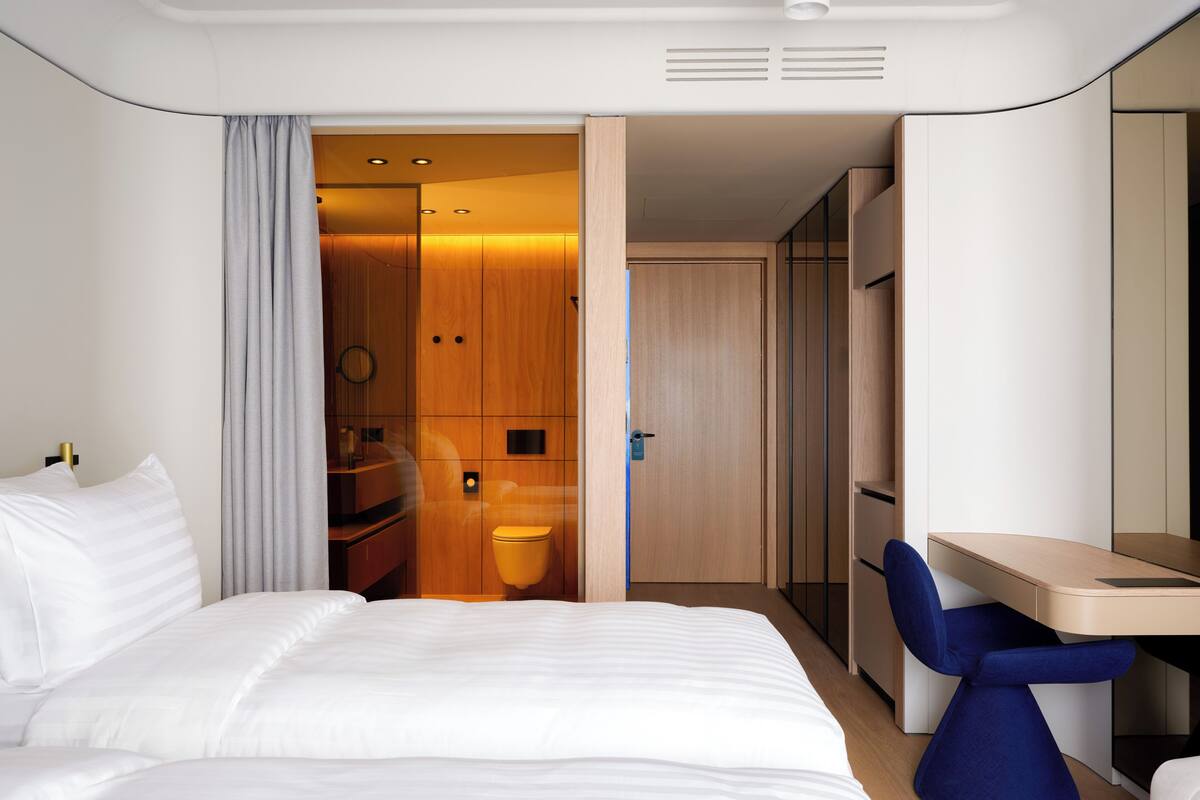 Una habitación de hotel moderna con una cama, un escritorio y un baño visible a través de una puerta abierta.