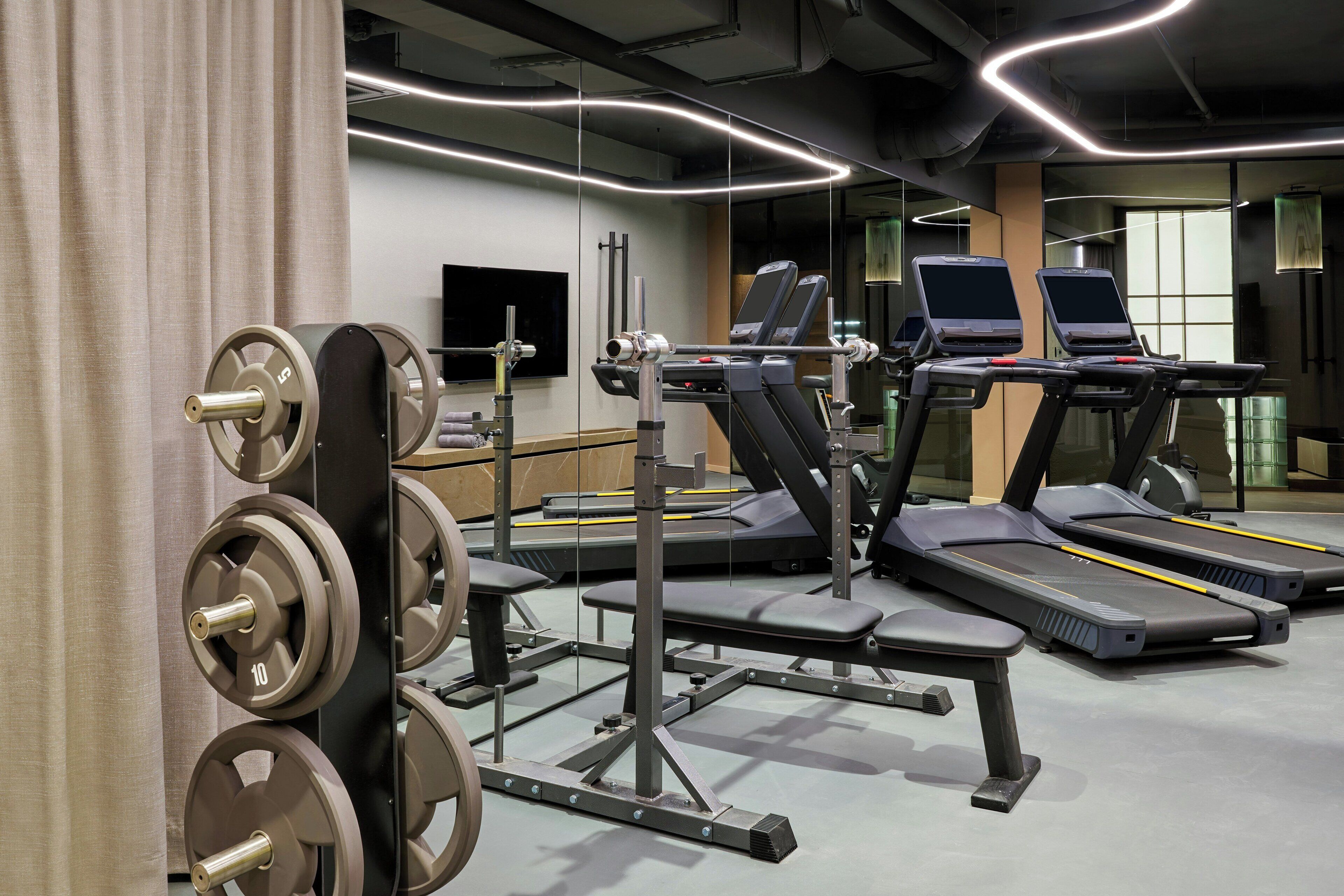 Une salle de sport équipée de tapis de course, de matériel de musculation et d’un mur recouvert de miroirs.