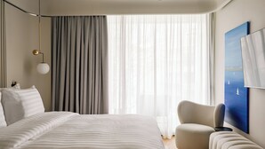 Quarto de hotel moderno com uma cama grande, um sofá, uma poltrona, um quadro e uma luminária no teto.