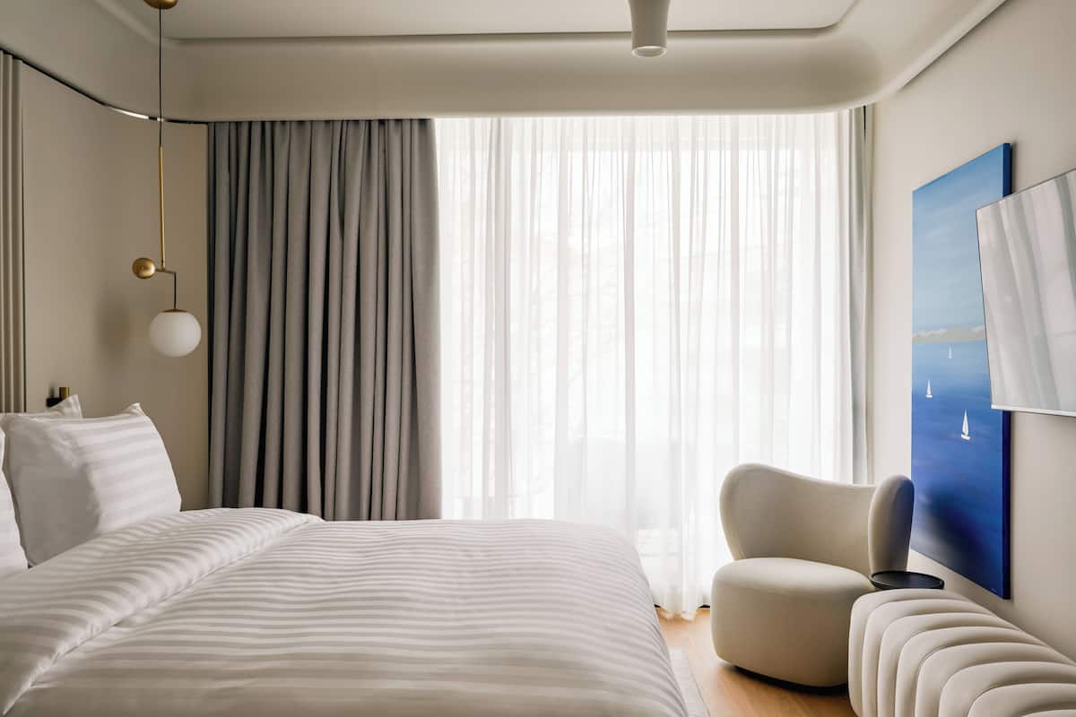 Una habitación de hotel moderna con una cama grande, un sofá, una silla, un cuadro y una lámpara en el techo.