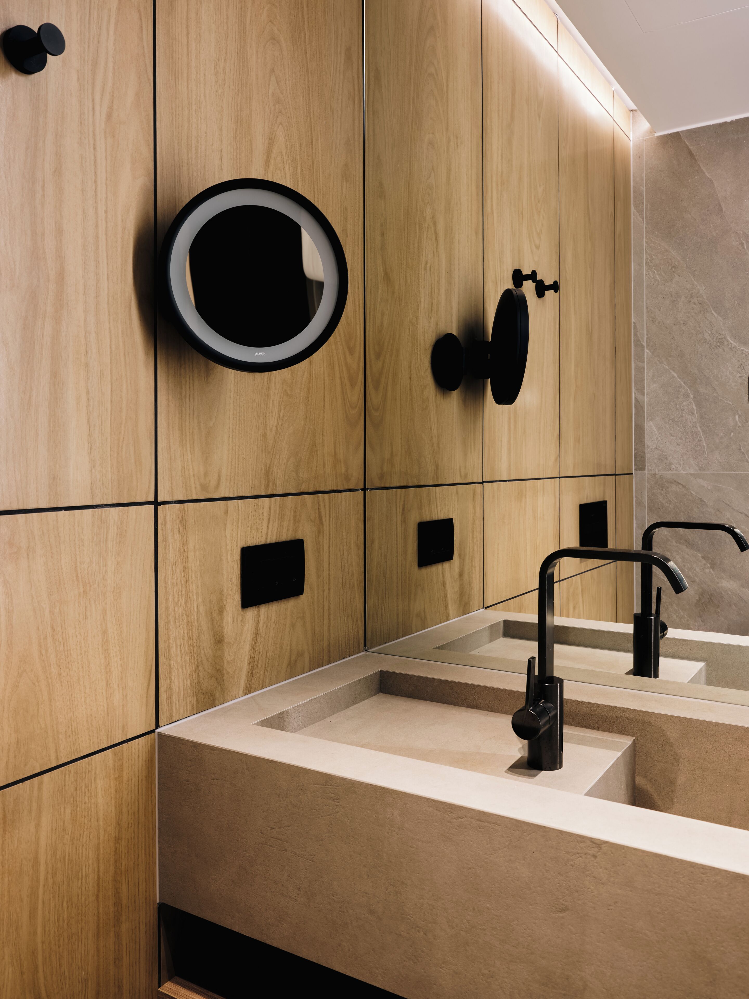 A modern bathroom with wooden paneling, a round mirror, and black fixtures.
