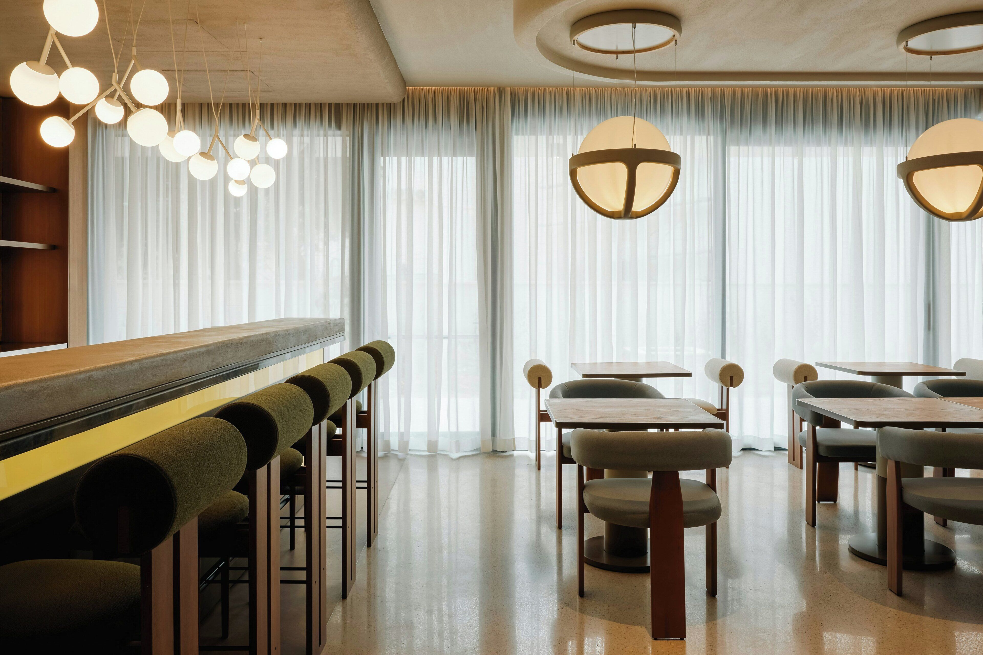 A modern dining area with bar seating, tables, and pendant lighting.